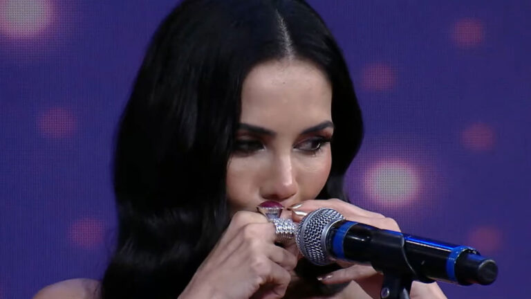 Daniela Albuquerque de cabelos pretos e longos toca gaita de boca segurando o instrumento com as mãos durante programa na RedeTV!