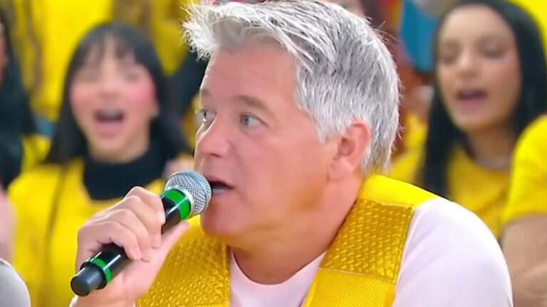 David Cardoso Jr. de cabelos grisalhos fala ao microfone vestindo colete amarelo brilhante durante participação em programa de TV