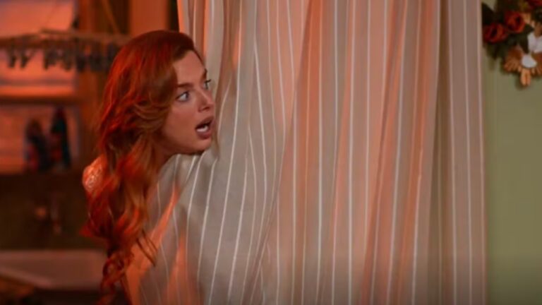 A imagem mostra uma mulher de cabelos ruivos espiando assustada por trás de uma cortina listrada em tons claros. Ela está com a boca aberta, aparentando surpresa ou medo, e o ambiente ao fundo parece ser uma casa, com decoração simples e iluminação quente.