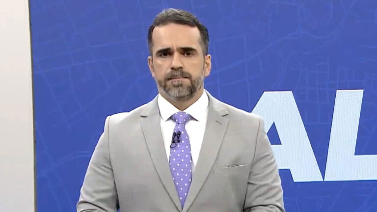 Jornalista Filipe Toledo, âncora do AL2, de barba, terno cinza claro e gravata lilás estampada no estúdio da TV Gazeta de Alagoas