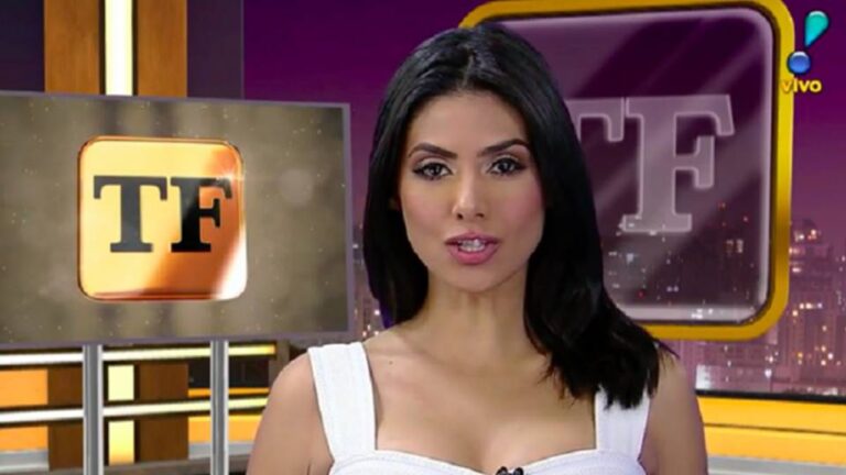 Apresentadora de telejornal em estúdio olha diretamente para a câmera. Ela tem cabelo preto liso, na altura dos ombros, e veste um top branco sem mangas. Ao fundo, aparecem telas com o logotipo “TF” em destaque e cenário em tons de roxo e dourado, além da indicação de transmissão ao vivo no canto superior da imagem.