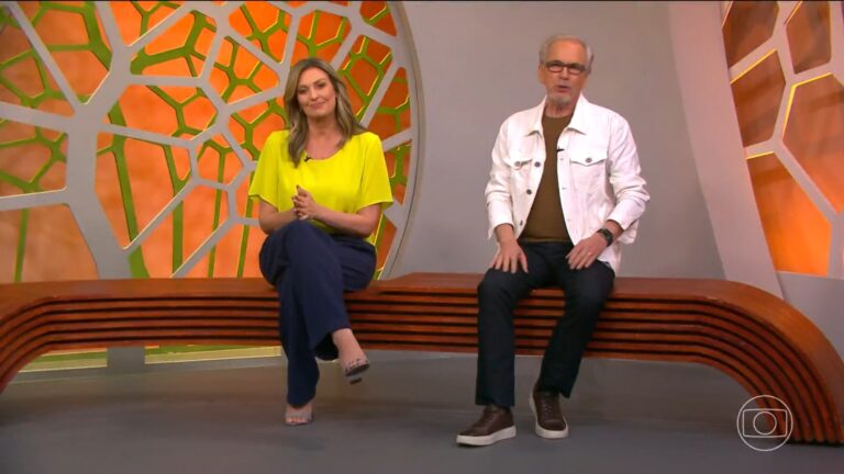 A imagem mostra Cristina Vieira e Nélson Araújo sentados em um banco de madeira curvado no estúdio do programa Globo Rural. O cenário tem tons quentes de laranja e verde, com um painel decorativo geométrico ao fundo. Ambos sorriem enquanto conversam, em um ambiente acolhedor e descontraído típico do programa matinal
