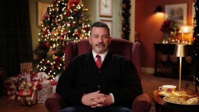 Homem sentado em poltrona com roupa social e gravata vermelha em sala decorada com árvore e presentes de Natal