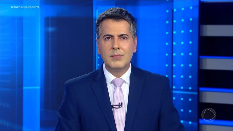 A imagem mostra Clébio Cavagnolle, um apresentador de telejornal em um estúdio iluminado com tons de azul. Ele veste terno azul-escuro, camisa branca e gravata lilás clara, com expressão séria enquanto encara a câmera. No canto superior esquerdo aparece a hashtag do Jornal da Record, identificando o programa jornalístico