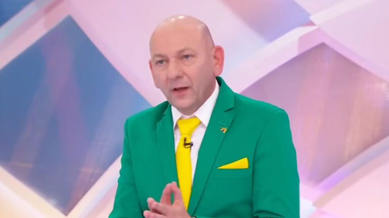 Luciano Hang com terno verde e gravata amarela no palco do Programa Silvio Santos em estúdio do SBT