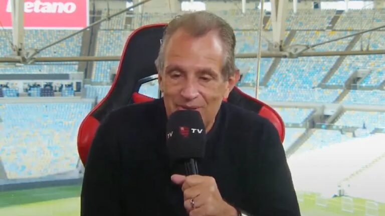 Homem com microfone da FlaTV fala em transmissão esportiva no estádio do Maracanã com arquibancadas ao fundo