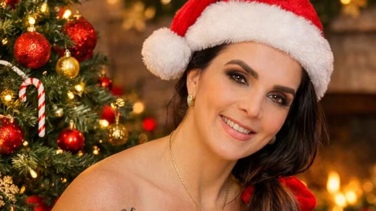 Luiza Ambiel sorridente usando gorro de Papai Noel com árvore de Natal decorada ao fundo em ensaio fotográfico especial de Natal