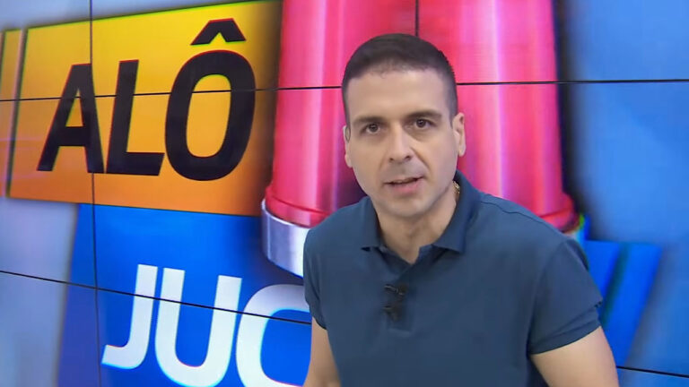 Marcelo Castro com camisa azul escura e colar, olhando para a câmera, com o logo do programa Alô Juca ao fundo