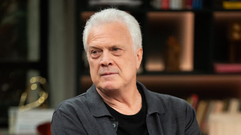 Pedro Bial de camisa cinza e cabelos brancos com expressão séria no cenário do programa Conversa com Bial nos estúdios da Globo