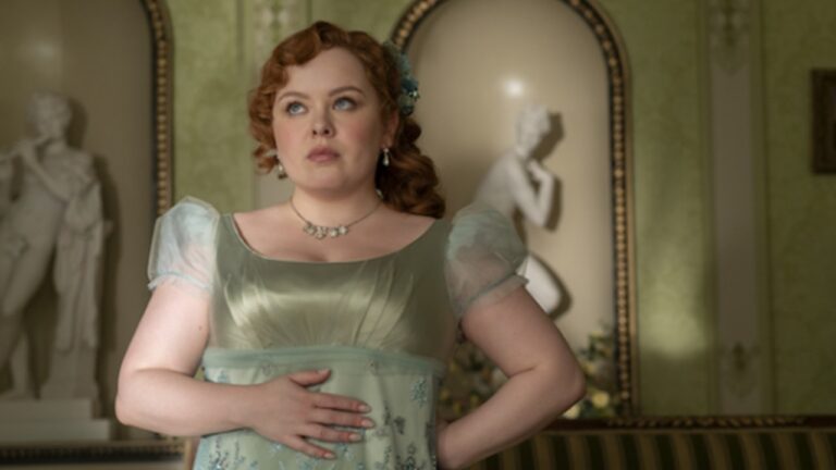 Penelope Featherington usa vestido verde de época com mão sobre o abdômen em sala clássica com esculturas ao fundo