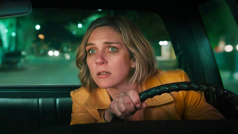 Mulher com expressão assustada dirige carro à noite segurando firme o volante com rua iluminada desfocada ao fundo