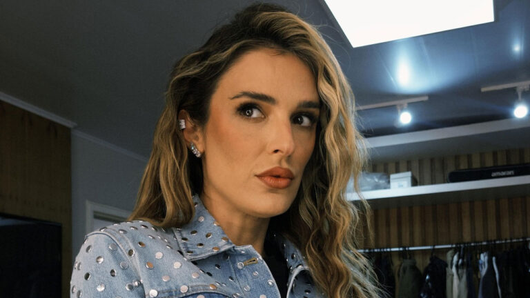 Rafa Brites veste jaqueta jeans com tachas e cabelo ondulado ao olhar para o lado em camarim iluminado durante bastidores de foto