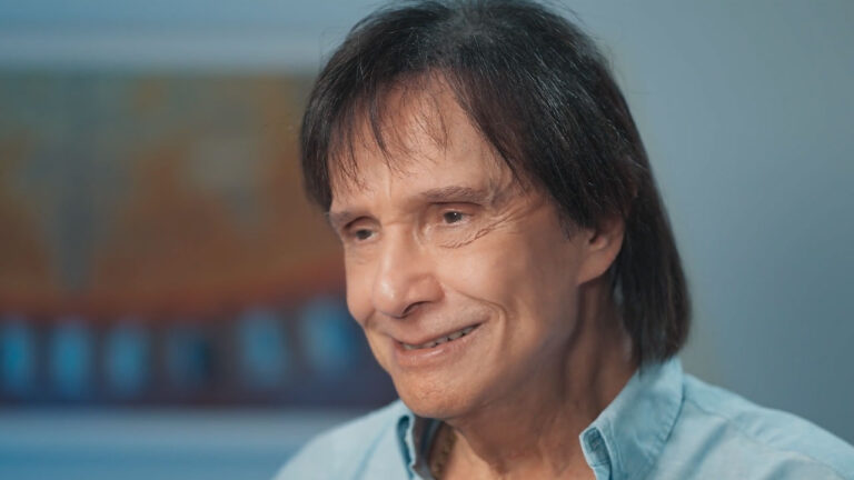 Roberto Carlos sorri usando camisa azul clara durante entrevista