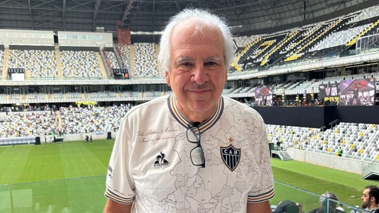 Homem idoso de cabelos brancos veste camisa do time Atlético Mineiro e posa sorrindo em estádio com arquibancadas e gramado ao fundo