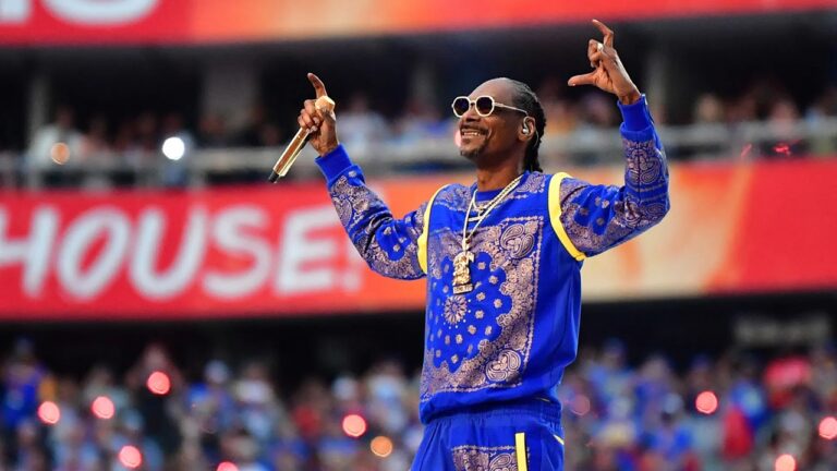 Snoop Dogg se apresenta em estádio com microfone dourado e óculos escuros vestindo conjunto azul diante do público