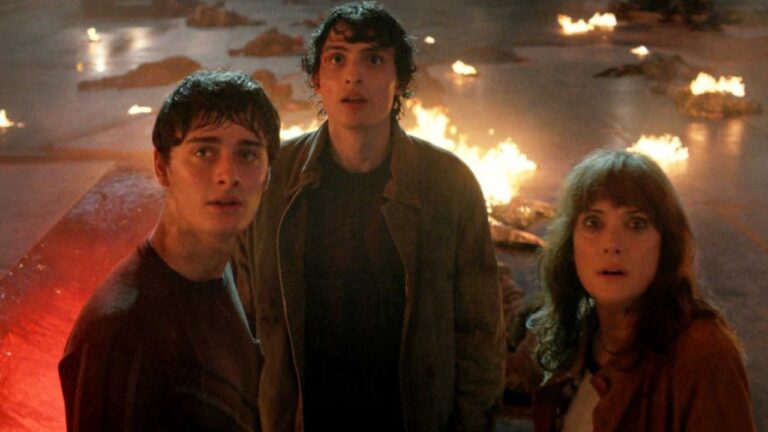 Dois rapazes e uma mulher com expressão de espanto observam algo em ambiente escuro com fogo ao redor
