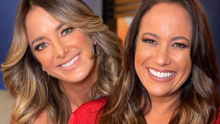 Duas mulheres sorridentes com cabelos soltos e roupas vermelhas posam lado a lado em estúdio de televisão