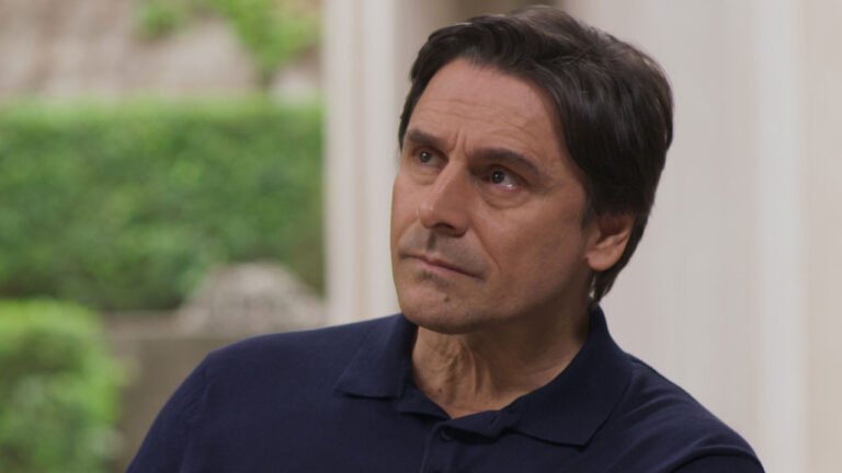 Murilo Rosa como Tomás Argento na novela Beleza Fatal da Max usa camisa polo azul escura com expressão séria em ambiente externo