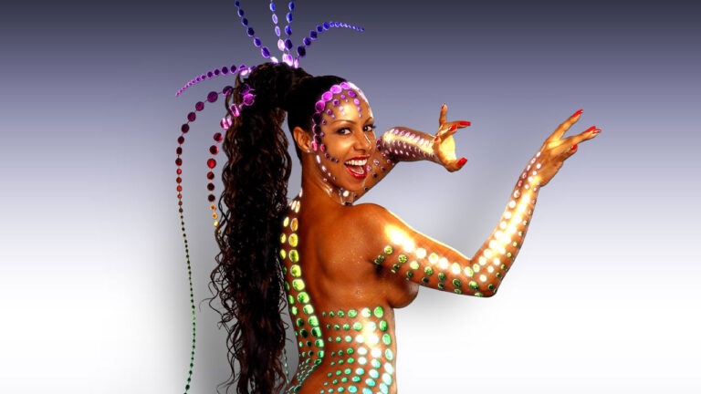 Valéria Valenssa como Globeleza sorrindo de corpo pintado com círculos coloridos e braços esticados em fundo degradê