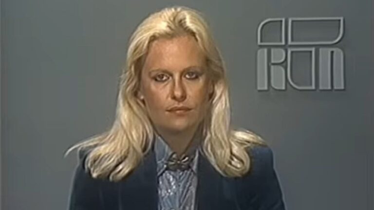 Mulher loira de expressão séria aparece em um estúdio de telejornal com fundo cinza e o logotipo da emissora à direita. Ela veste camisa azul clara com laço no pescoço e blazer azul escuro, em uma imagem com aparência antiga e iluminação típica de transmissões de TV das décadas passadas.