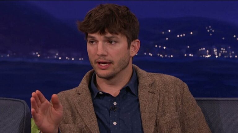 Homem de blazer marrom e camisa azul fala gesticulando durante entrevista em programa de TV noturno