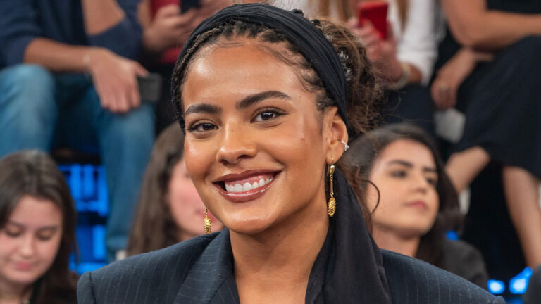 Bella Campos sorri com faixa preta no cabelo e brincos dourados durante sua participação no programa Altas Horas nos estúdios da Globo