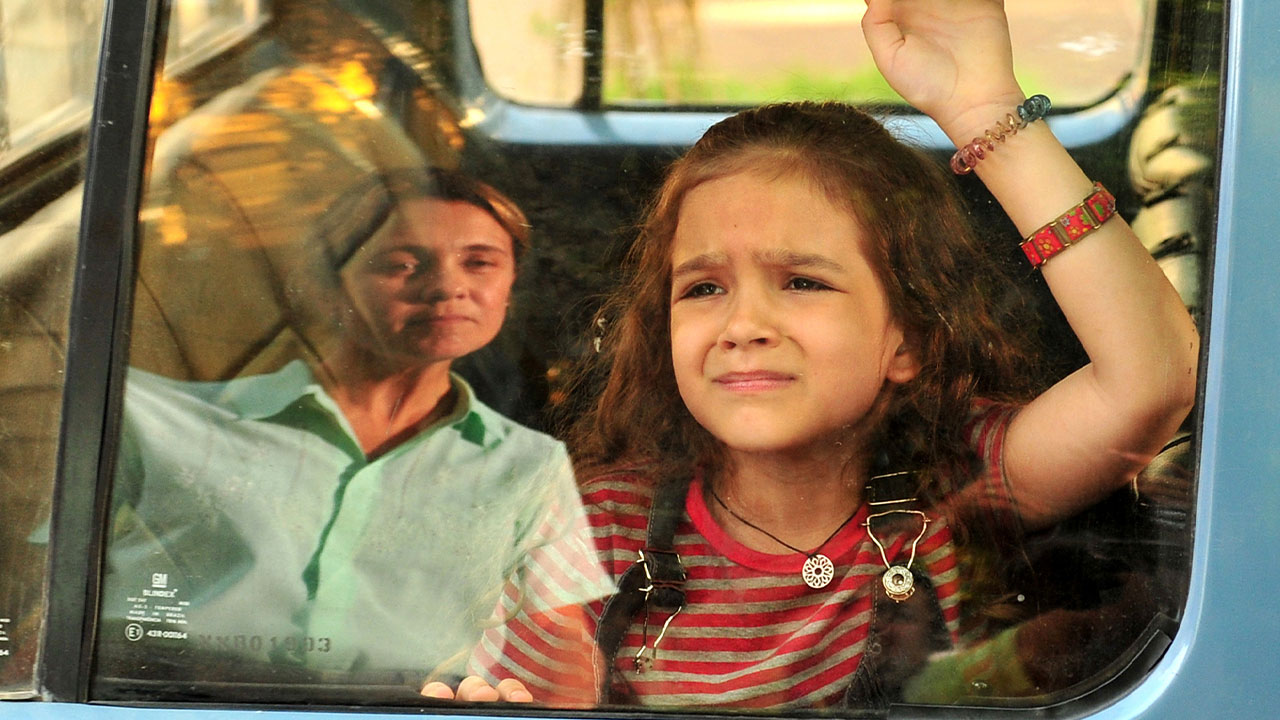 Rita (Mel Maia) chora na janela de um carro enquanto Carminha (Adriana Esteves) observa com desdém em cena da novela Avenida Brasil