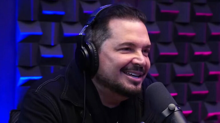 Cantor Conrado sorri usando fones de ouvido e jaqueta escura durante entrevista em estúdio de podcast com isolamento acústico ao fundo