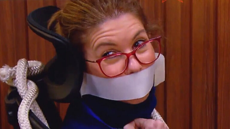 Daniela Beyruti amarrada em cadeira com fita na boca e óculos vermelhos durante gravação do piloto do Comédia SBT em estúdio
