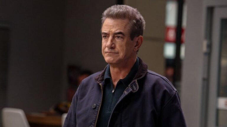 Homem de expressão séria usa jaqueta escura em cena ambientada em local interno iluminado