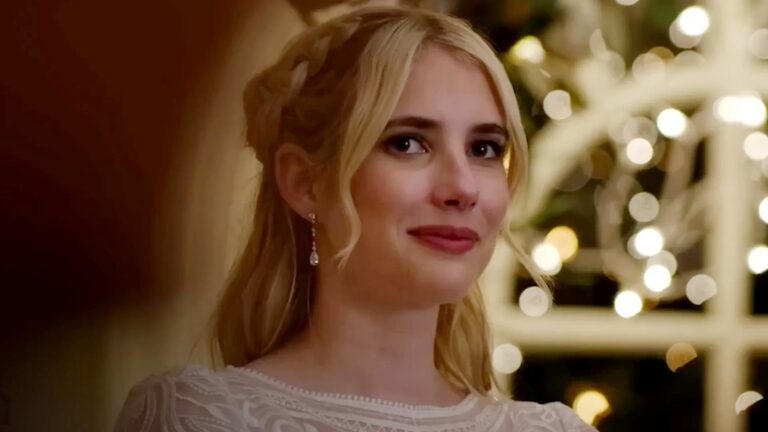 A imagem mostra Emma Roberts, uma mulher loira com expressão serena, usando um vestido branco rendado e brincos delicados. Seu cabelo está parcialmente preso com tranças, e o fundo exibe luzes desfocadas e douradas, criando um clima romântico e festivo em uma cena do filme Destinos Traçados, da Sessão da Tarde