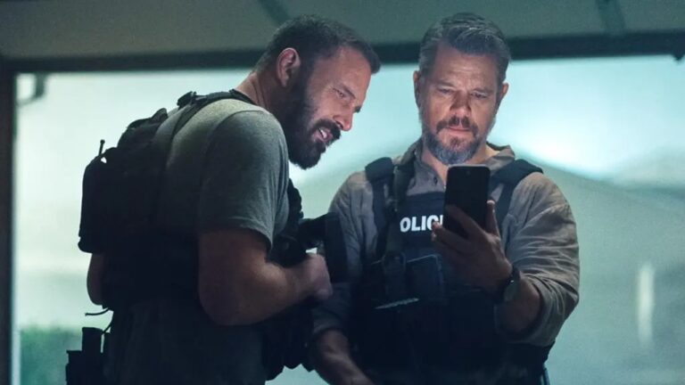 Dois policiais com coletes táticos observam tela de celular durante operação em ambiente interno com iluminação fria e clima de tensão