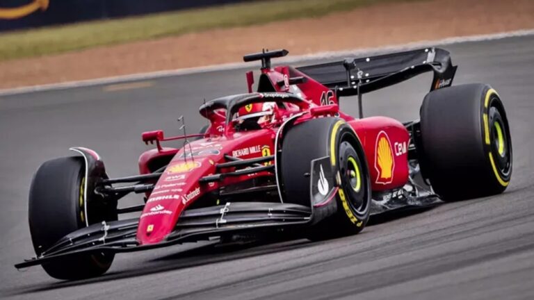 Carro de Fórmula 1 vermelho da equipe Ferrari em alta velocidade em pista de corrida, com o número 16 visível na frente e logotipos de patrocinadores como Shell e Santander nas laterais, pneus Pirelli e o piloto usando capacete dentro do cockpit.