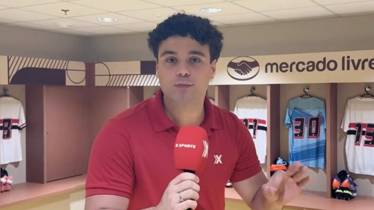 Gabriel Guimarães segura microfone da Xsports em vestiário com camisas de futebol ao fundo e logotipo do Mercado Livre na parede