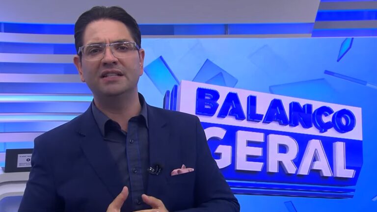 A imagem mostra Guilherme Rivaroli no estúdio do programa Balanço Geral, exibido pela RIC Record. Ele usa terno azul escuro, camisa da mesma cor e lenço rosa no bolso. Ao fundo, o logotipo do programa aparece em letras tridimensionais azuis sobre um painel iluminado em tons de azul e branco