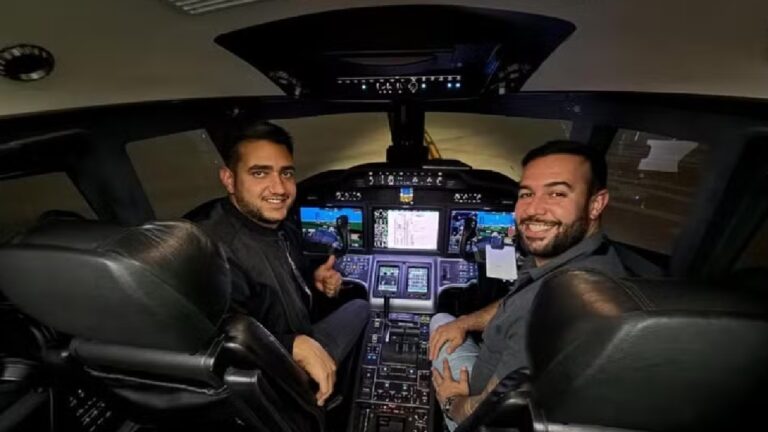 Dois pilotos sorriem na cabine de comando de um avião, cercados por painéis iluminados e controles de voo