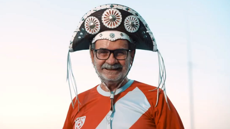 Torcedor de barba, óculos e chapéu de couro sorri com camisa vermelha e branca em chamada da Copa do Nordeste exibida no SBT