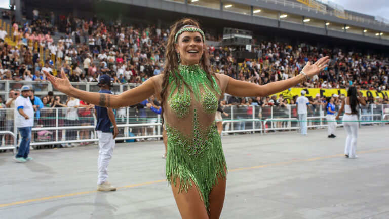 Josi Aoas desfila com fantasia verde brilhante de samba de braços abertos em avenida com arquibancadas lotadas