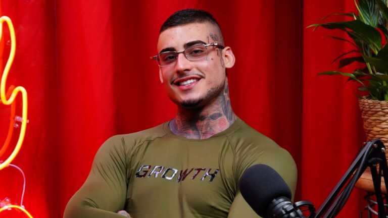 Kylian Cria sorri com óculos e braços cruzados vestindo camiseta verde da Growth durante gravação de podcast em estúdio com fundo vermelho