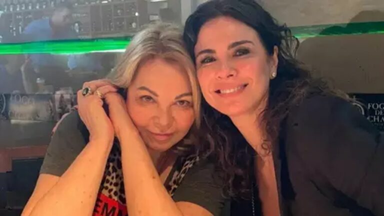 Duas mulheres sorriem abraçadas sentadas em mesa de restaurante iluminado