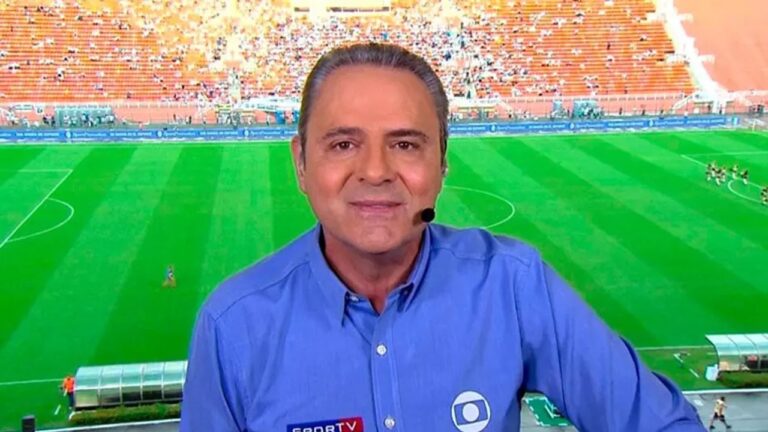 Luis Roberto com camisa azul da Globo e microfone comenta partida em estádio de futebol com gramado verde e arquibancadas cheias ao fundo