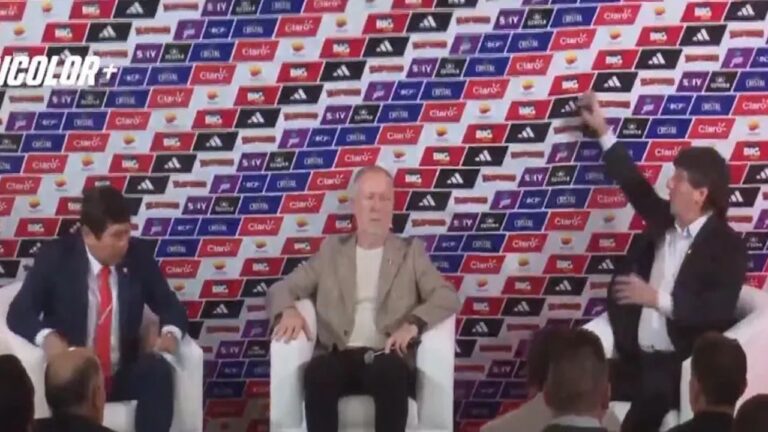 A imagem mostra uma coletiva de imprensa, com três homens sentados em poltronas brancas diante de um painel repleto de logotipos de patrocinadores esportivos, como Adidas, Claro e Cristal. O homem ao centro parece ser o foco do evento, enquanto o da direita gesticula em direção ao painel.