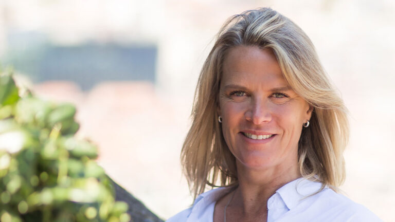 Mariana Becker sorridente com camisa branca e cabelos loiros soltos em ambiente externo