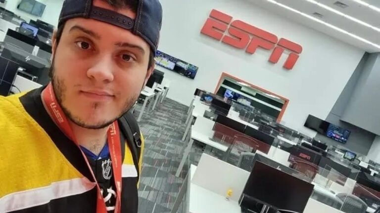 Homem tira selfie em redação da ESPN, vestindo boné para trás, crachá vermelho e camisa esportiva amarela