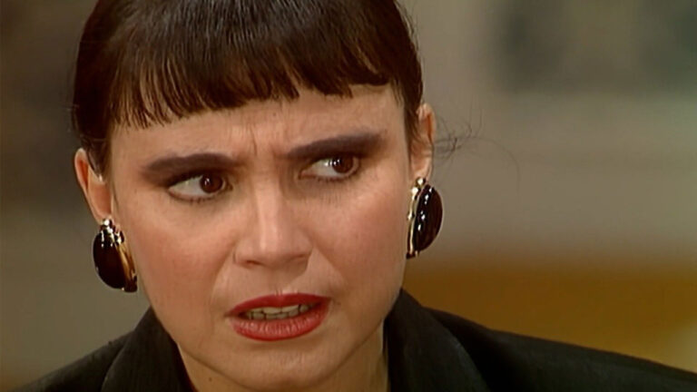 Regina Duarte como Maria do Carmo com expressão de preocupação e brincos grandes em cena da novela Rainha da Sucata na Globo