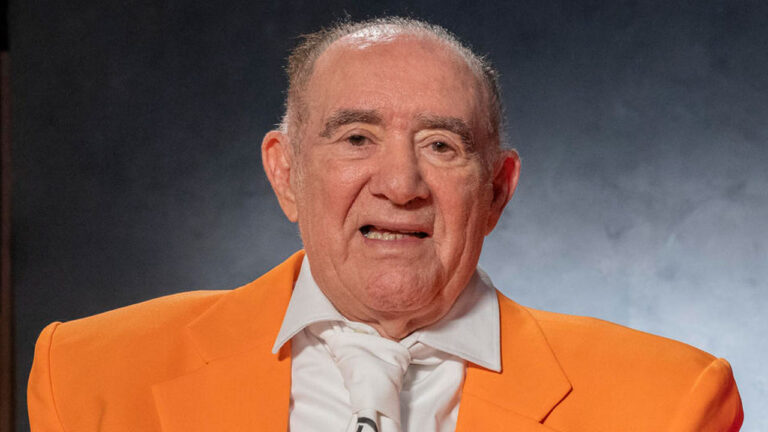 Renato Aragão sorri usando terno laranja e gravata branca caracterizado como Didi em gravação do especial de 60 anos da Globo