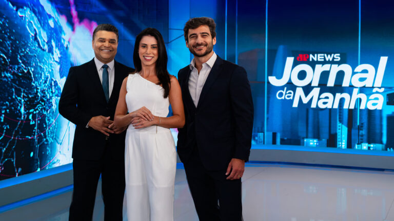 Roberto Nonato, Beatriz Frehner e Evando Cini sorridentes no estúdio do Jornal da Manhã da Jovem Pan News com logotipo ao fundo