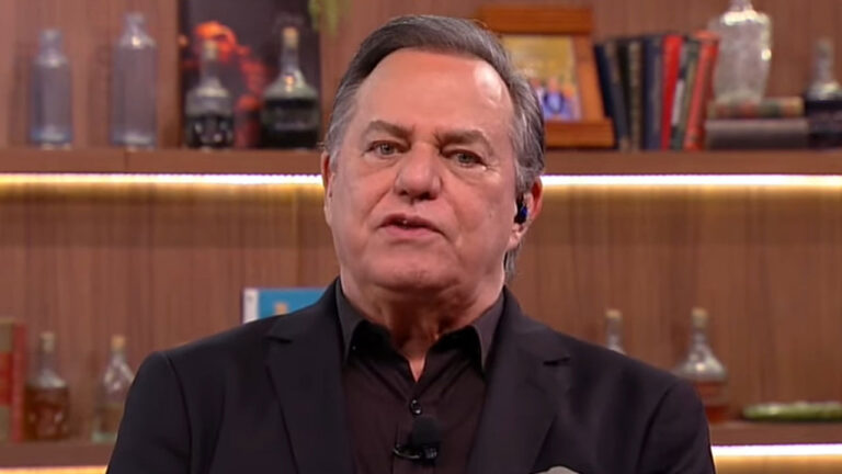 O apresentador Ronnie Von de terno preto e camisa escura fala no programa Companhia Certa da RedeTV em cenário com estantes de madeira e garrafas