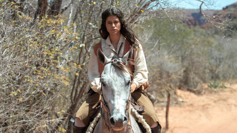 Rosa (Isadora Cruz) monta cavalo branco em meio à vegetação seca da caatinga na novela Guerreiros do Sol