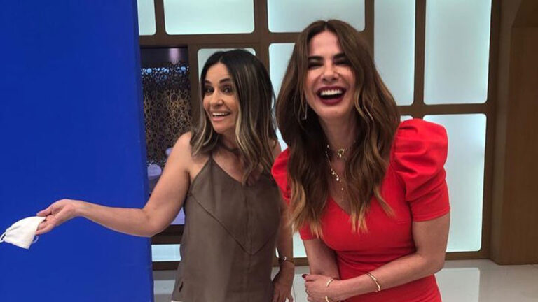 Simone Garuti e Luciana Gimenez sorriem juntas nos bastidores do Superpop na RedeTV! com Luciana usando um vestido vermelho vibrante